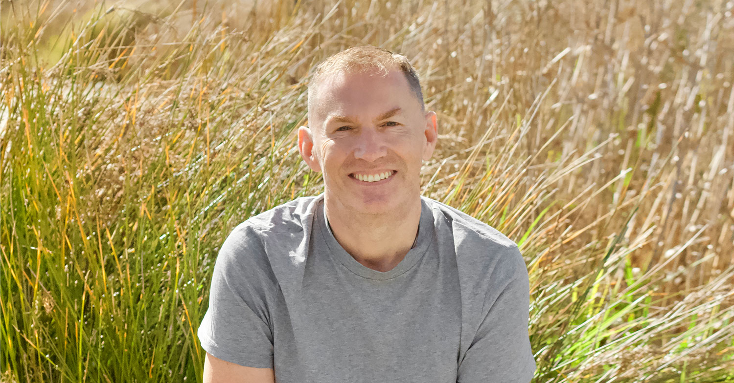 Tim Antric smiles at the camera. Behind him as a sea of grasses.